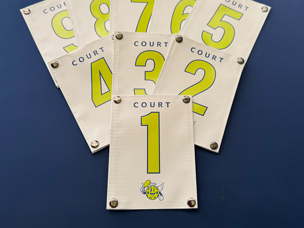 Lime green custom pickleball court ID number signs for a tournament, showing Court numbers in bold print