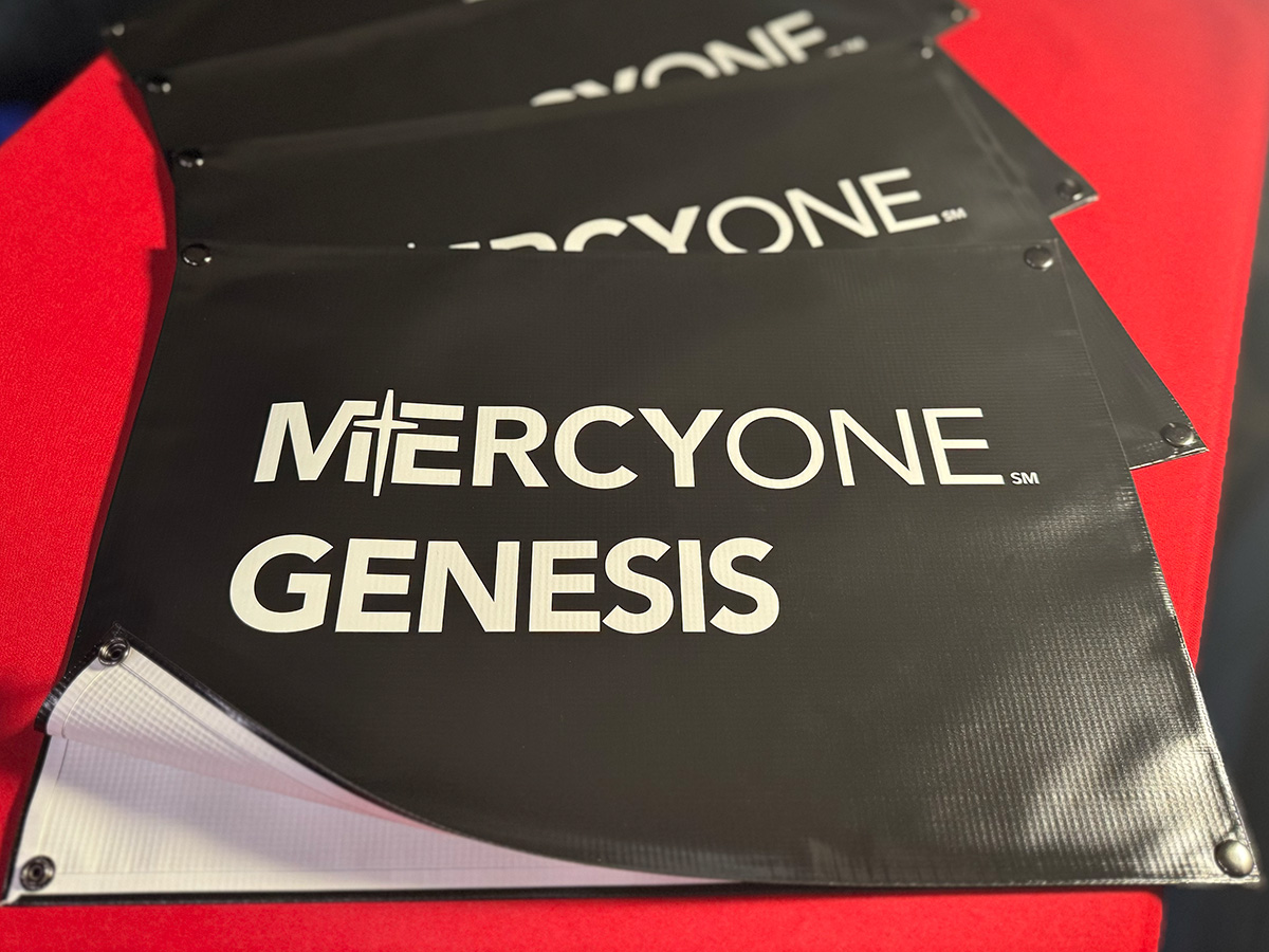 Stack of finished MercyOne Genesis snap-on net banners ready to ship